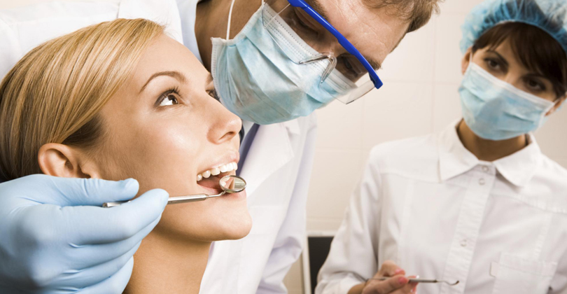 Picture of a dentist with a dental assistant, representing the dental care available in San Jose, Costa Rica.  The picture shows the dentist checking his patient's mouth.