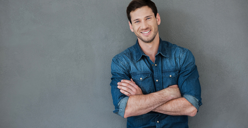 Picture of man standing with arms folded, representing the dental procedures available for males with Frontline Dental CR, San Jose, Costa Rica.  The man is wearing a blue shirt and is smiling while facing the camera.