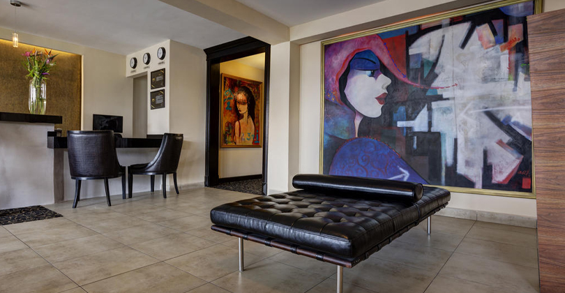 Picture of the lobby of the Costa Rica Medical Center Inn, San Jose, Costa Rica.  The picture shows a large mural on the wall and modern black furniture in the foreground.
