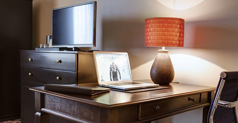 Picture of the desk area in the Jr. Suite of the Costa Rica Medical Center Inn, San Jose, Costa Rica.  The picture shows an executive desk and chair lamp, chest of drawers and a wide screen TV.